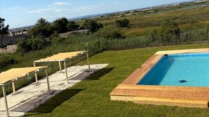 Piscina con muelle de madera, rodeada de césped y vistas a campos lejanos bajo un cielo despejado.