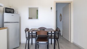 Una cocina compacta con microondas y refrigerador, una mesa de comedor con sillas, un espejo y una puerta adornada con un arreglo floral.