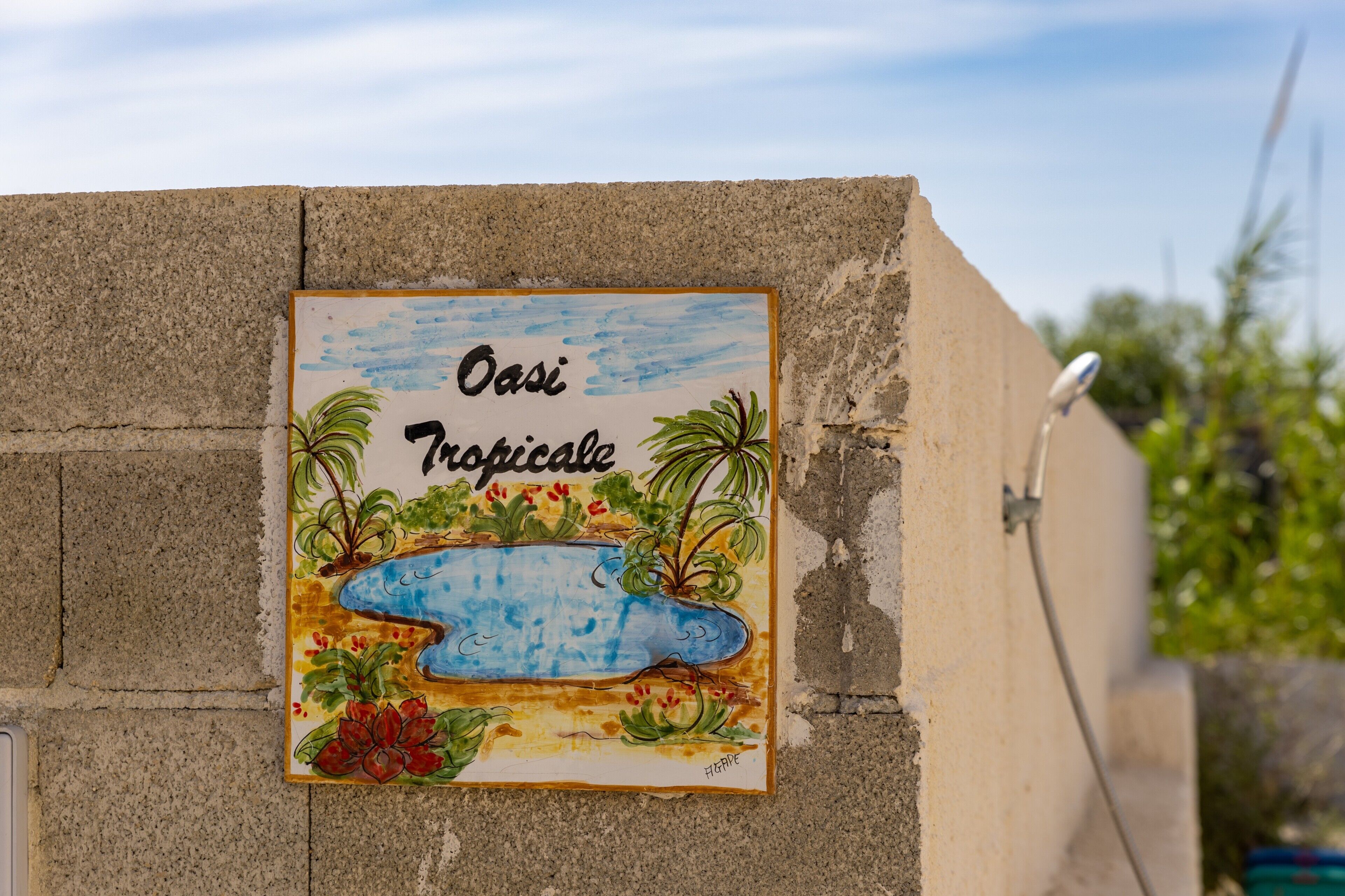 Un letrero con el texto 'Oasi Tropicale' en una pared de concreto.