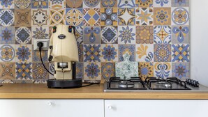 Una cocina con cafetera, estufa a gas y un salpicadero de azulejos estampados.