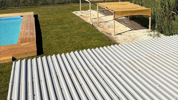 Una piscina con terraza de madera, zona de estar cubierta y vista a un paisaje natural.