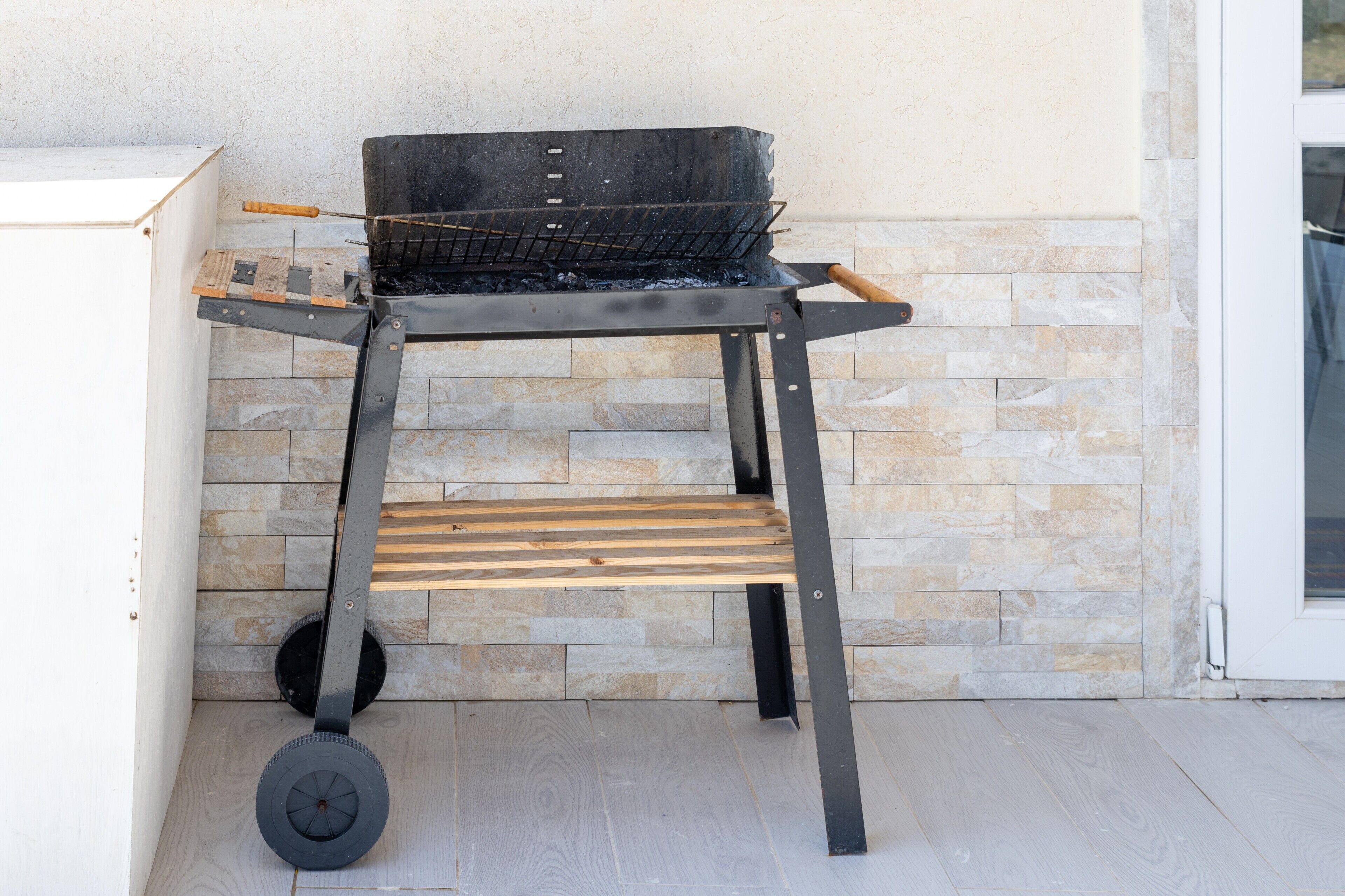 Una parrilla portátil con ruedas, ubicada junto a un muro de piedra.