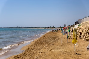 Ein sandiger Strand mit blauem Himmel, einer Felswand und einigen Sonnenschirmen.