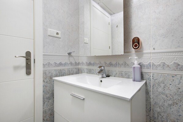 Casa de banho com lavatório branco, espelho e azulejos de mármore.