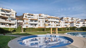 A residential building complex with multiple balconies, a swimming pool, and a well-maintained lawn.