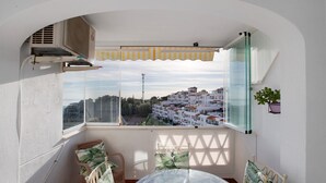 A balcony with a table and chairs, a potted plant, and a view of a town.