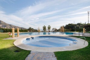 Une piscine bordée d’un chemin de pierre, avec des palmiers et une montagne en arrière-plan.