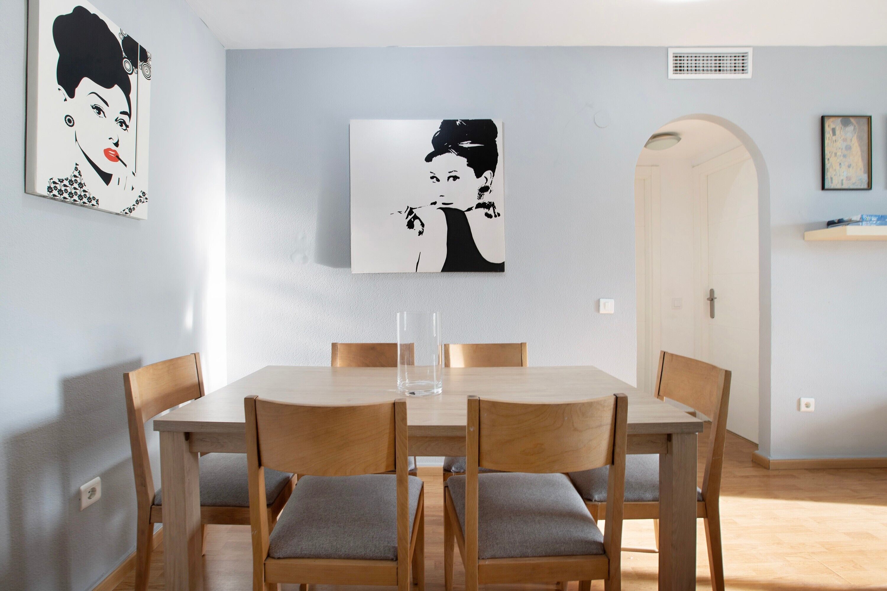 Un comedor con una mesa y sillas de madera, una obra de arte en la pared y una puerta que da a otra habitación.