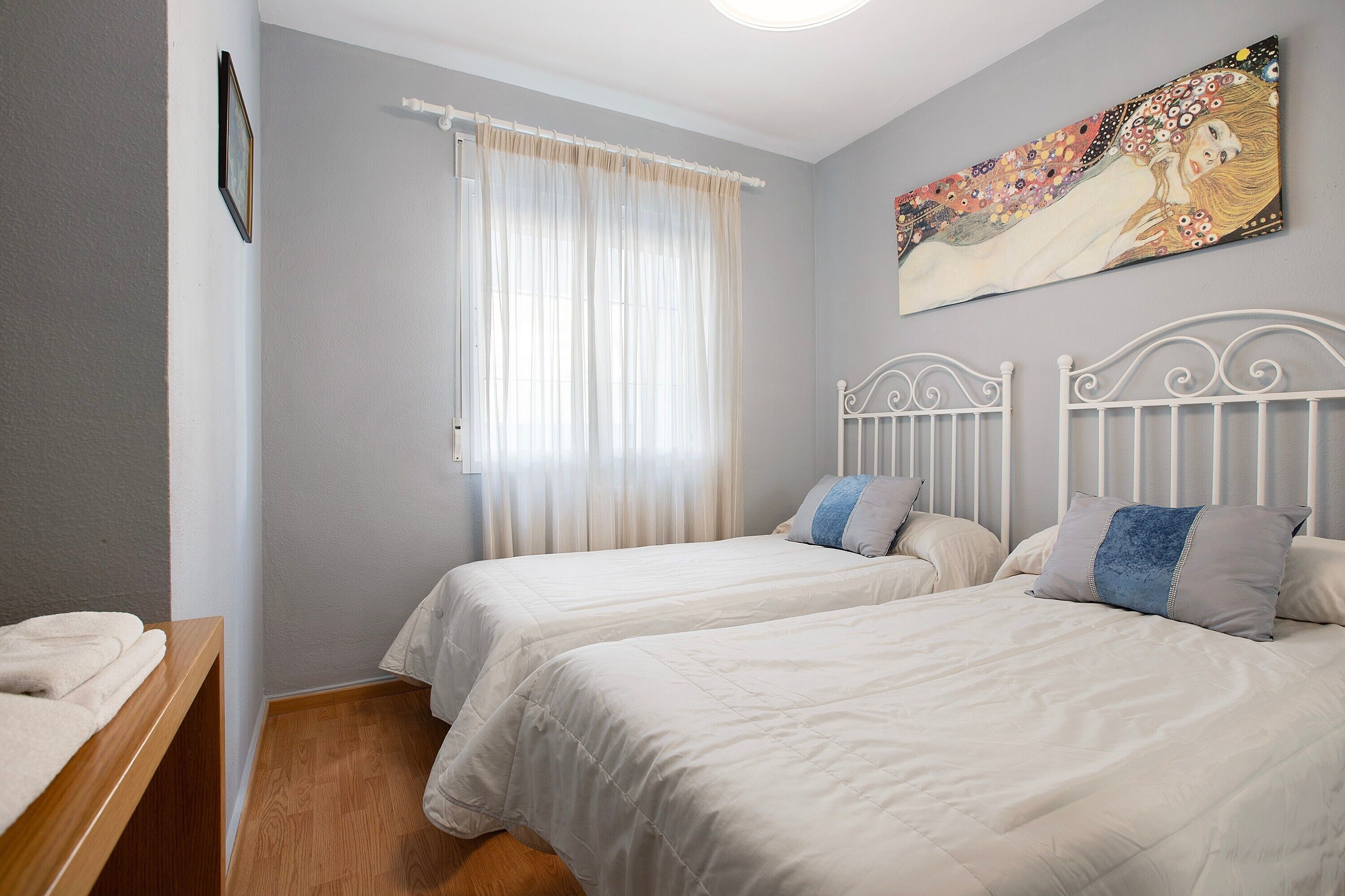 Une chambre avec deux lits, un tableau, une fenêtre avec des rideaux et un plancher en bois.