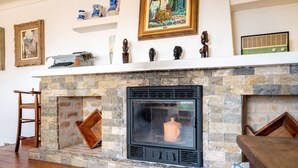 Une cheminée avec des murs en pierre, un fauteuil en bois et divers objets décoratifs disposés sur des étagères.