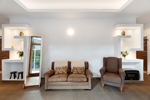 A modern living room with a sofa, armchair, built-in shelving, and a view through a glass door.