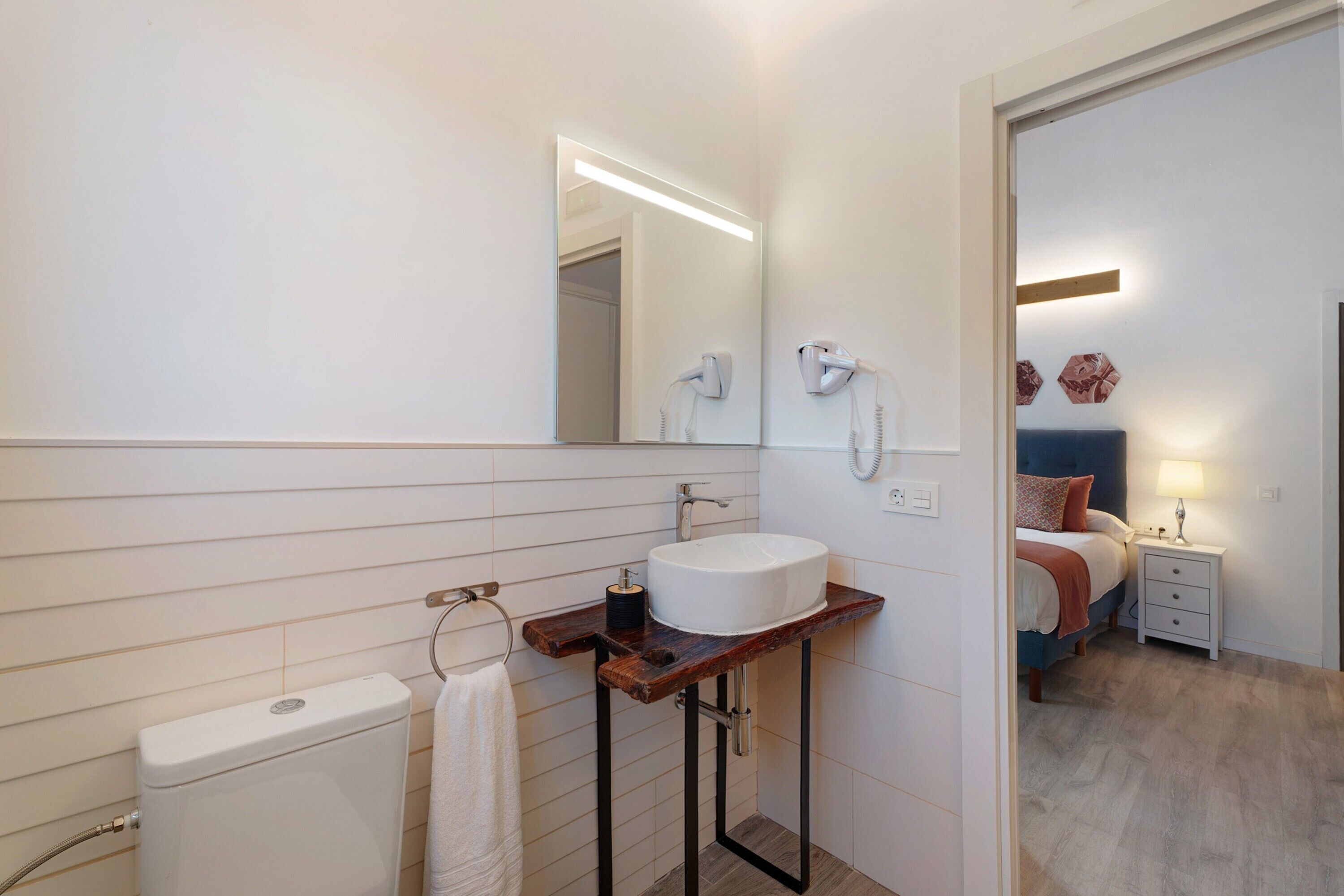 Ein Badezimmer mit Toilette, einem Holzkosmetikschrank mit Waschbecken, einem Handtuchhalter und einem Spiegel.