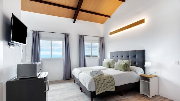 Une chambre d’hôtel moderne, dotée d’un grand lit, d’une télévision, d’un bureau et offrant une vue sur le ciel.