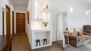 Et moderne interiør med en trædør mærket 'D', en hvid væg med hylder, en sofa med puder og en hængestol.