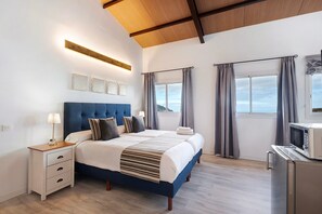 Une chambre à coucher comprenant un lit, des tables de chevet, une commode, une fenêtre avec des rideaux et un four à micro-ondes.