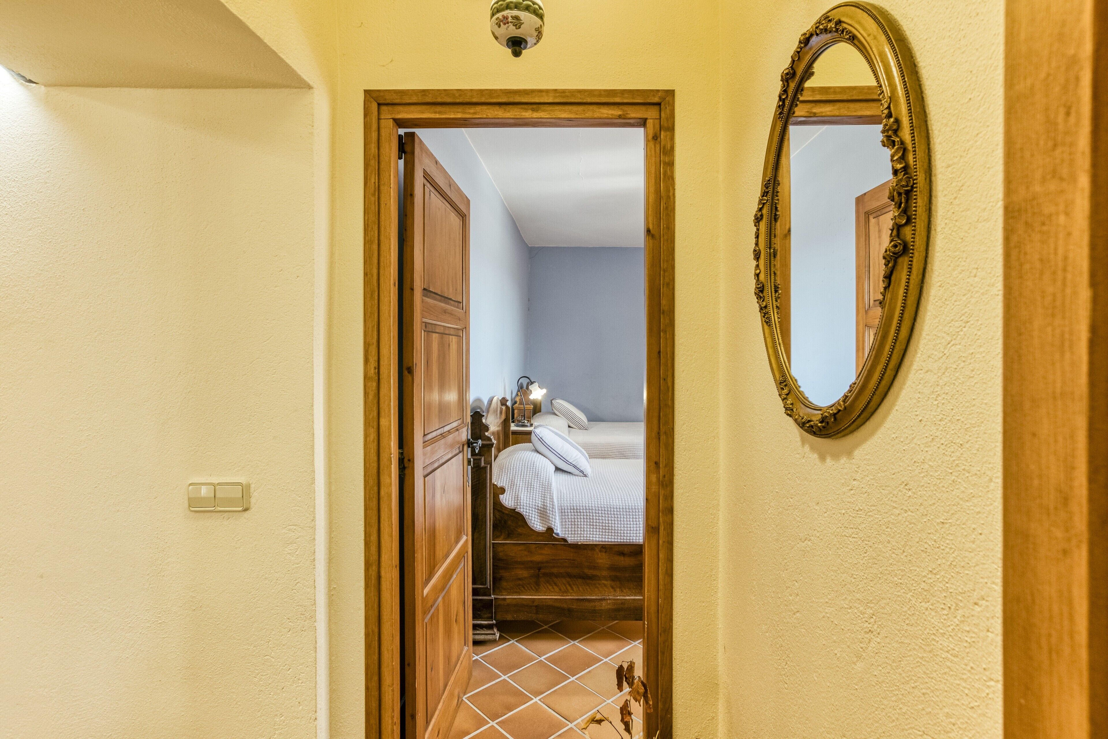 A doorway leading to a bedroom with a bed, a nightstand, and a mirror on the wall.