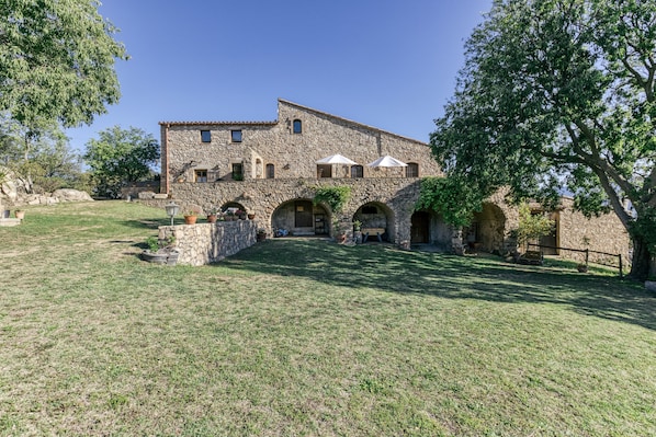A stone building with a central courtyard, arched doorways, and a large tree.
