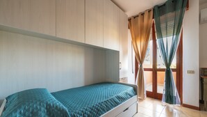 Una cama individual con cubierta acolchada, un armario de madera y una puerta corredera con cortinas.