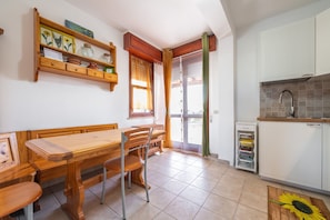 A kitchen with a wooden table and chairs, a built-in shelf with decorative items, and a tiled floor.