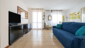 Una sala de estar con una televisión de pantalla plana, un sofá, una silla y un espejo decorativo.
