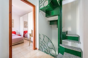 A bedroom with a bed, a chair, and a staircase with green railings.