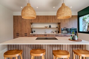 Een moderne keuken met houten kastjes, een groot eiland met barkrukken en hangende rieten hanglampen.