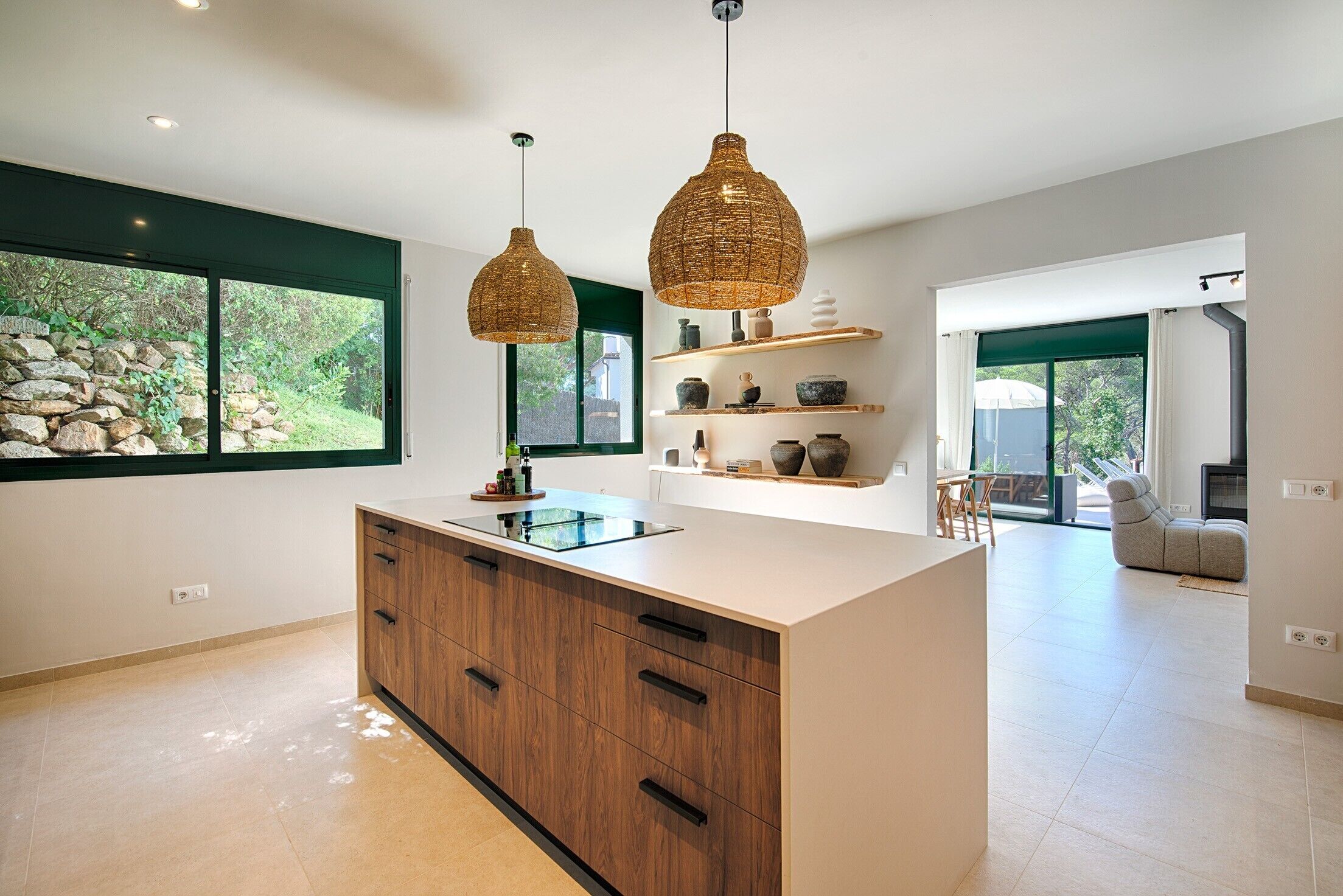 Een moderne keuken met een centraal eiland, hanglampen en uitzicht op groen.