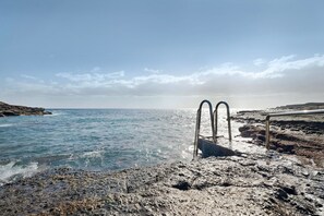Ein felsiger Strand mit klarem, blauem Wasser und einer Metallkonstruktion.