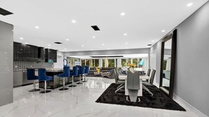 A modern kitchen with dark cabinets and a black backsplash, a dining area with a white table and grey chairs, and a living room with a grey sofa and a coffee table. - BEST LOCATION, Few min walk, Bike to Deerfield Beach and Pier. one acre property (Deerfield Beach)