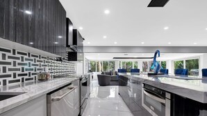 A modern kitchen with a marble countertop, dark cabinetry, and a view of the outdoors through large windows. - BEST LOCATION, Few min walk, Bike to Deerfield Beach and Pier. one acre property (Deerfield Beach)