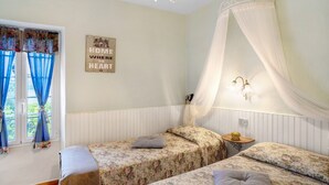 A bedroom with two beds, a window with blue curtains, a wall-mounted light, and a sign that reads 'HOME WHERE THE HEART IS.' - Apartment 'Casa Cen' with Sea View, Private Terrace and Wi-Fi (Dolcedo)