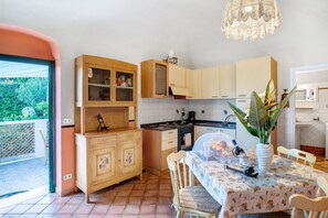 Een keuken met houten kastjes, een eettafel met een bloemendessin en een hanglamp.