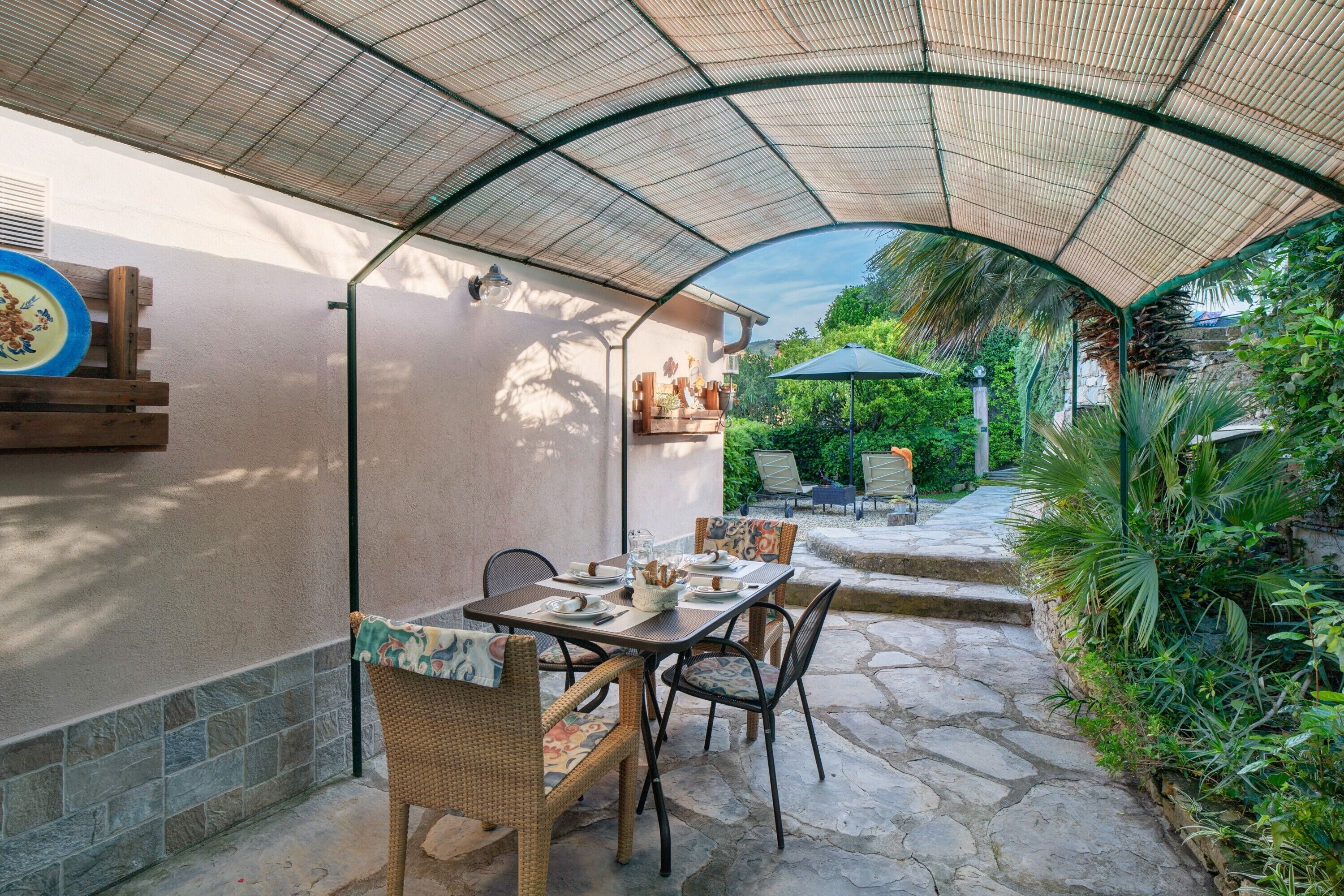 Une terrasse extérieure dotée d’un espace salon abrité, d’un sol en pierre et d’une végétation luxuriante.