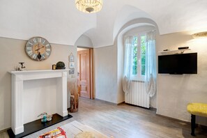 Una habitación con chimenea blanca, un reloj de pared, un televisor y un banco.