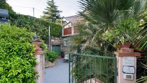 Un étroit sentier mène à une maison dotée d’un portail vert, entourée d’une végétation luxuriante et d’un mur de pierre.