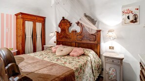 Une chambre à coucher avec un lit en bois, une table de chevet, une commode, une chaise, une armoire et une lampe fixée au mur.