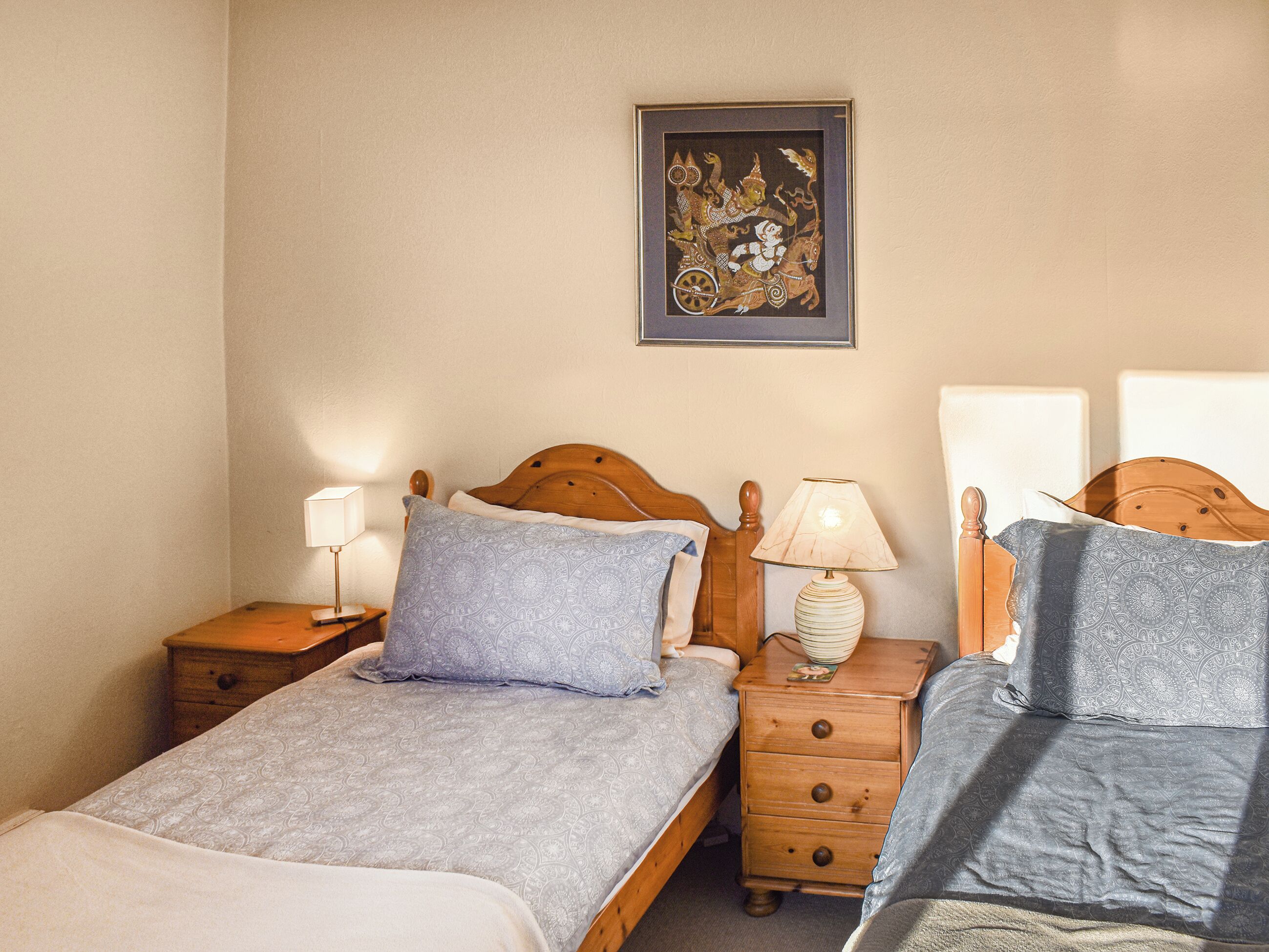 Un dormitorio con dos camas individuales, cabeceras de madera, mesitas de noche con lámparas y un cuadro enmarcado en la pared.