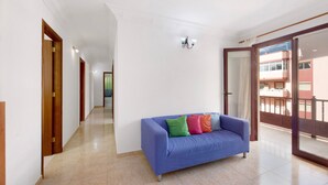 Un salón con un sofá azul, una araña y vistas de un edificio a través de un ventanal.