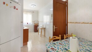 Una habitación con cama, puerta de madera, zona de cocina con refrigerador y baño con ducha.
