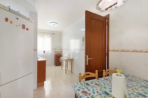 A room with a bed, a wooden door, a kitchen area with a refrigerator, and a bathroom with a shower.