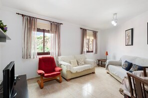 A living room with a TV, two sofas, a red chair, and curtains.