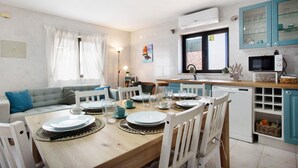 A dining area with a wooden table set for four, white chairs, and a kitchen with teal cabinets and a microwave.