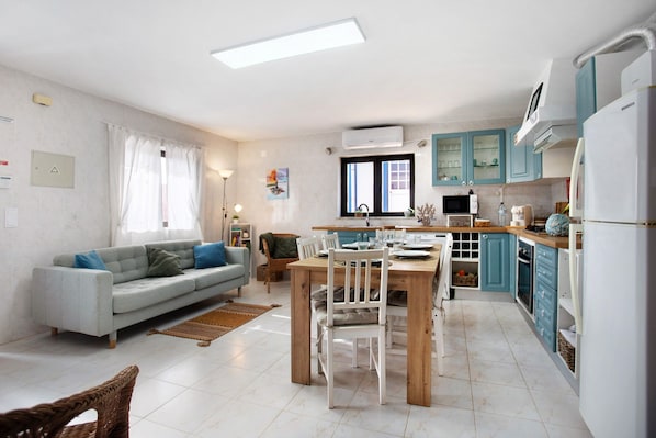 A modern kitchen with a dining area, a sofa, and a television.