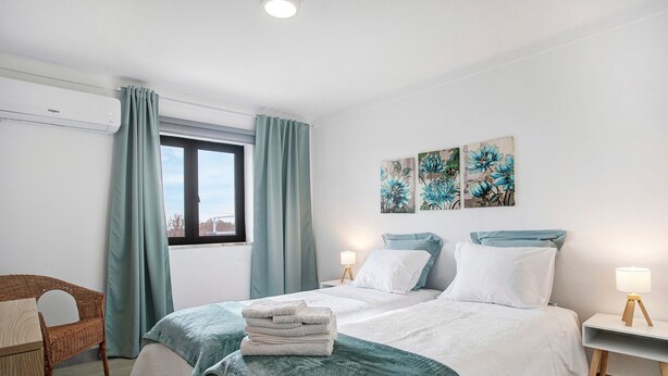 A bedroom with a bed, two bedside tables, a chair, and artwork on the wall.
