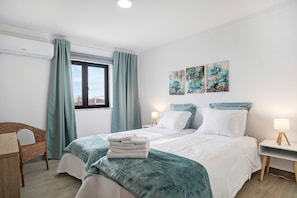 A bedroom with a bed, two bedside tables, a chair, and artwork on the wall.