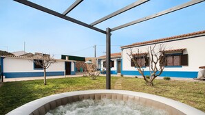 A hot tub in a courtyard with a metal pergola overhead, surrounded by buildings with blue trim and a clear sky.