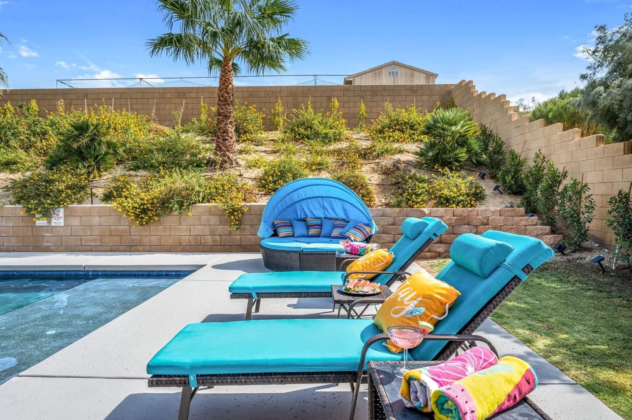 A poolside area with lounge chairs, a blue tent, and a brick wall backdrop.