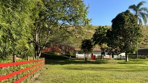 A grassy area with a red fence, trees, and a building in the background.