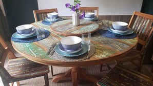 A round wooden dining table with blue and green patterned placemats, surrounded by wooden chairs.