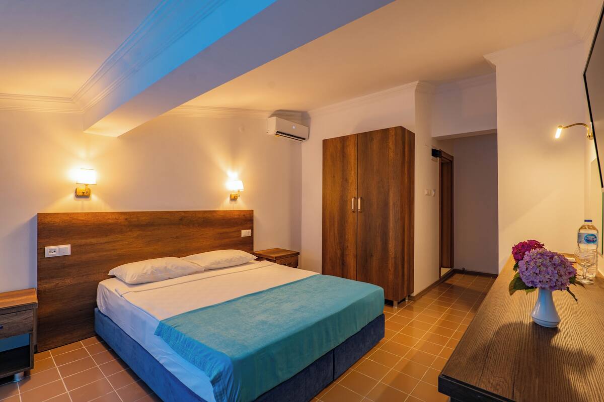 A bedroom with a wooden headboard, a bed with white linens, a nightstand, a wooden wardrobe, and a night lamp.